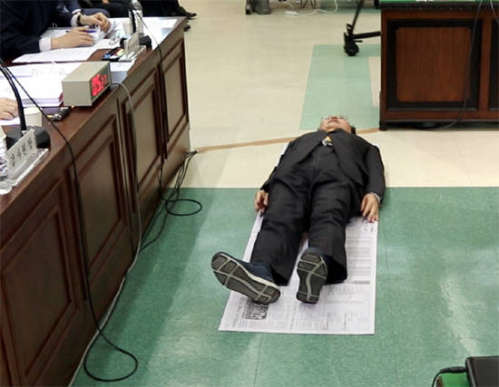 19일 국회 법사위원회 감사원 국정감사에서 노회찬 정의당 원내대표가 교정시설 수용자 1인당 평균 가용면적(약 0.3평)과 같은 크기로 이어 붙인 신문지 위에 드러누워 상황을 설명하고 있다. ⓒ 노회찬 의원실
