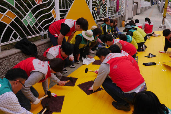 부산은행 희망드림봉사단이 성서초등학교 앞 횡단보도 노면에 '엘로카펫'을 설치하고 있다. ⓒ BNK