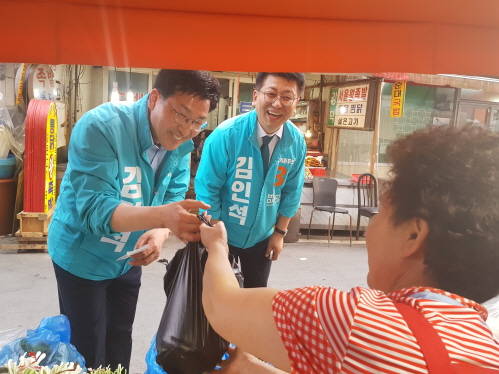 김광석 후보(왼쪽)가 남문시장 상인이 건네는 야채 봉투를 받아들고 있다. 오른쪽은 큰형이자 대구광역시의회에 출사표를 던진 김인석 후보. ⓒ 프라임경제