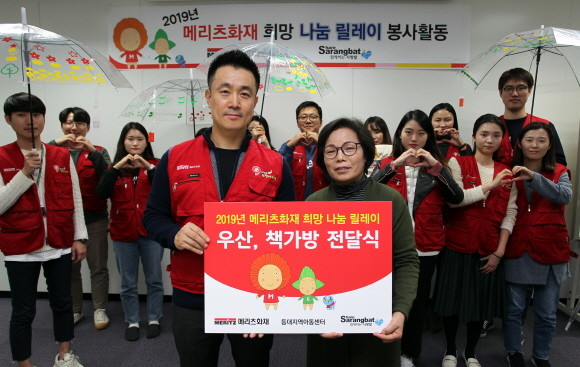 지난 26일 메리츠화재 임직원들이 투명우산 및 책가방을 만들어 중구 등대지역아동센터 김효순 센터장(오른쪽)에게 전달하고 있다. ⓒ 메리츠화재
