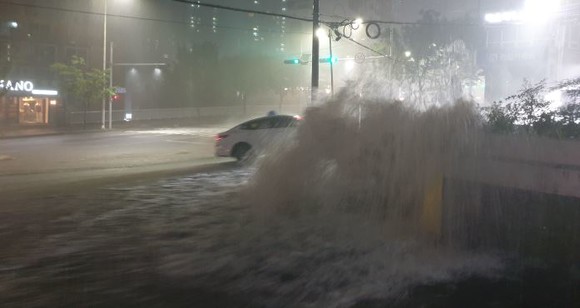 23일 시간당 80mm가 넘는 장대비가 쏟아져 부산 해운대구 중2동 달맞이 입구 도로가 역류한 물이 마치 폭포를 이루면서 그 옆을 지나가는 택시를 덮칠 듯 위협하고 있다. = 서경수 기자