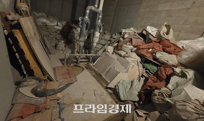 아파트 지하주차장의 한 공간에 시멘트가 담긴 포대, 타일 조각, 판자, 골판지 상자 등이 무질서하게 쌓여 있다. ⓒ 프라임경제