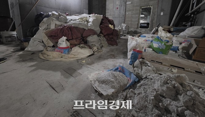 아파트 지하주차장의 한 공간에 시멘트가 담긴 포대, 타일 조각, 판자, 골판지 상자 등이 무질서하게 쌓여 있다. ⓒ 프라임경제