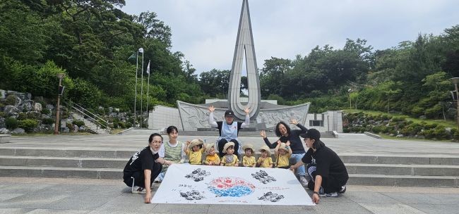 소라어린이집 원아들과 교사들이 충혼탑 앞에서 직접 준비한 '손도장 태극기'를 펼치며 나라를 위해 헌신한 분들의 숭고한 정신을 되새기며 기념 촬영을 하고 있다. ⓒ 소라어린이집