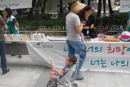  21일 하나생명 본사 앞에서 열린 바자회에서 한 시민이 아이에게 장난감을 사 주고 값을 치르고 있다. = 임혜현 기자