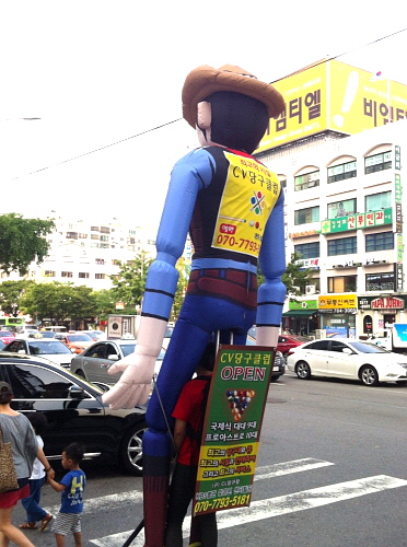  한 남성이 개업한 당구장을 홍보하기 위해 자신보다 2배 이상 큰 인형을 짊어진 채 횡단보도 앞에 서 있다. = 최민지 기자