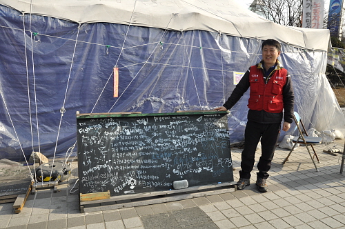  과천 코오롱그룹 본사 앞 천막 농성을 2년째 이어오고 있는 최일배 코오롱정투위 위원장. 칠판에는 인근 주민들이 남겨준 응원 글이 가득했다. = 이보배 기자